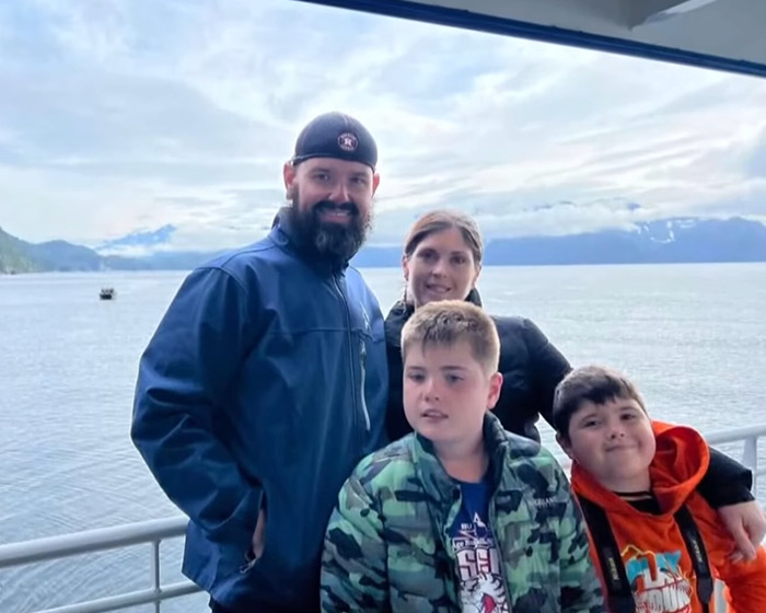 Family of four posing on a boat with scenic water and mountains, related to remains found after boating tragedy.