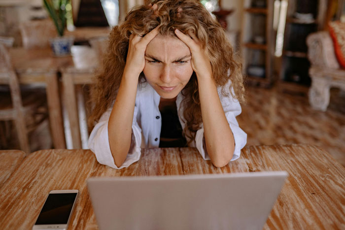 Woman looking stressed while using laptop at wooden table, relating to couple booking wedding venue years in advance dilemma.
