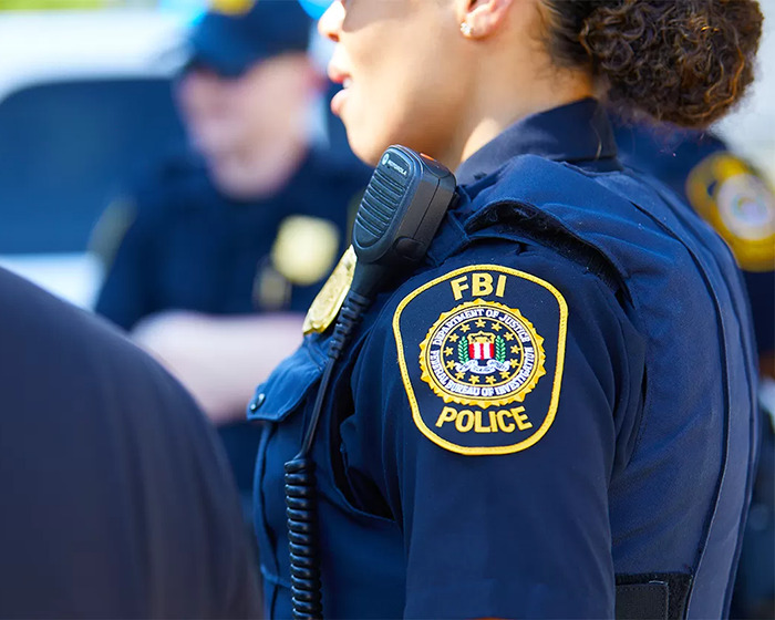 FBI police officer in uniform with badge and radio during law enforcement operation involving ICE agents.