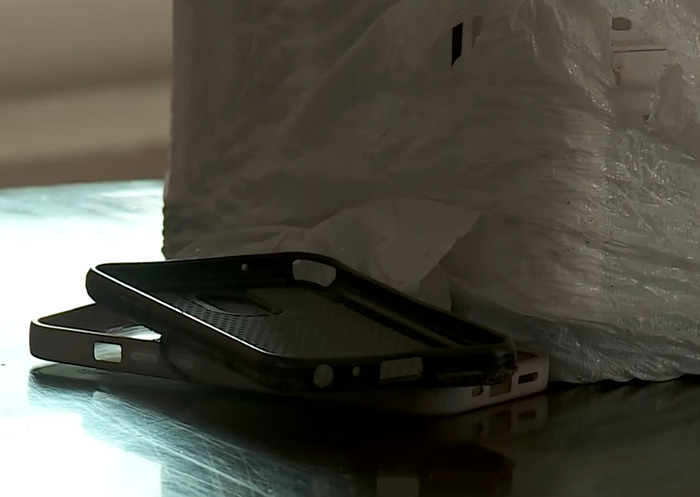 Black phone cases stacked on a reflective surface near a white textured object after ICE agents raid wrong home.