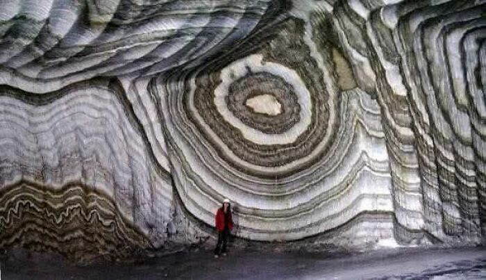 Person standing inside a cave with striking layered rock formations, showcasing nature’s breathtaking beauty.