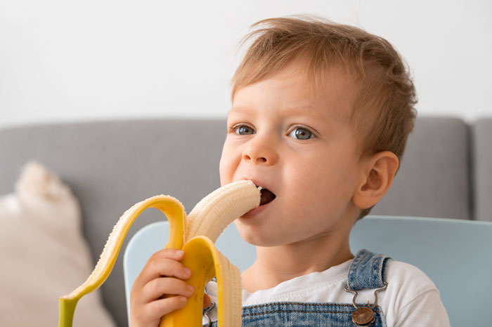 Toddler enjoying a peeled banana, showing a son's veggie love with healthy fruit over traditional meals.