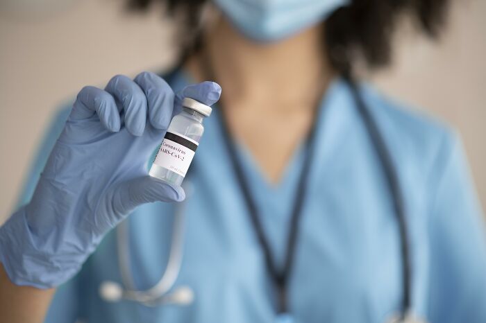 Healthcare worker in blue scrubs and gloves holding a coronavirus vaccine vial, relating to people who called off their wedding.