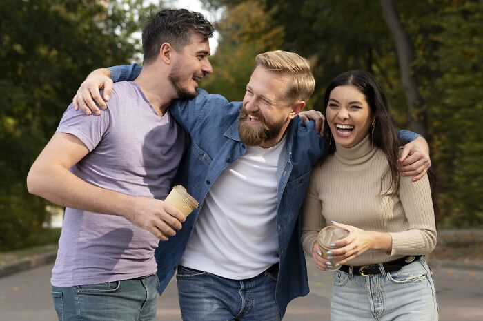 Three friends laughing and embracing outdoors, reflecting themes of lost friendships and ultimatums among men and women.