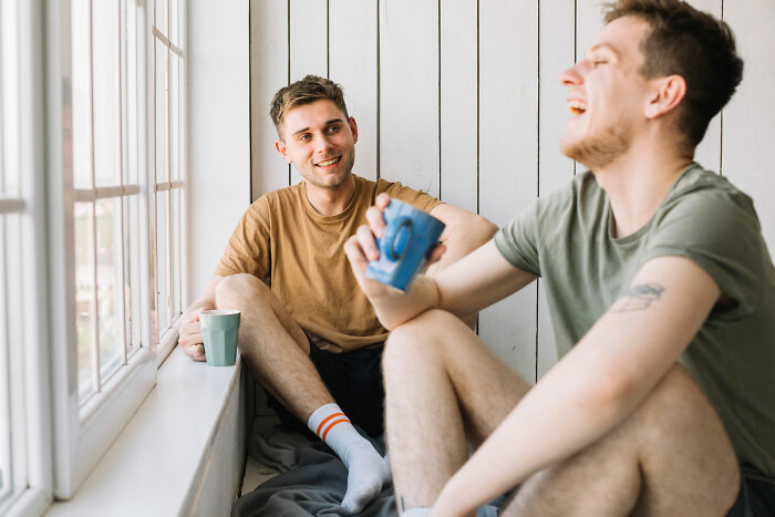 Two men sharing coffee and laughter by a window, representing lost friendships and ultimatums between male friends.