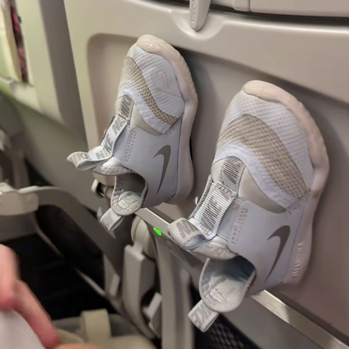 Baby's shoes stuck to airplane seat back during flight as a travel hack, sparking mixed reactions from passengers.