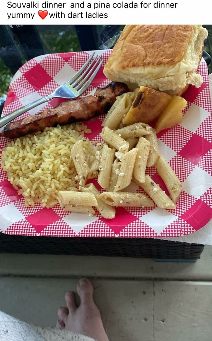Plate with souvlaki, rice, pasta, bread roll, and pineapple on a checkered paper plate with a fork, showing cursed food presentation.