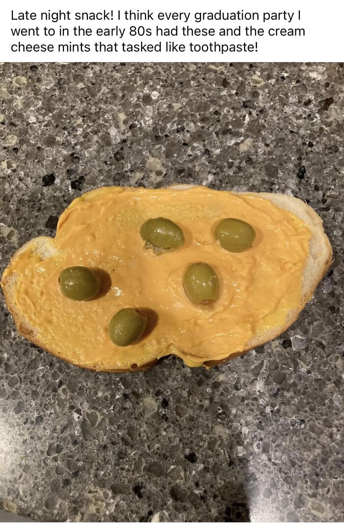 Slice of bread with orange cheese spread and green olives on a granite countertop, a cursed food pic example.