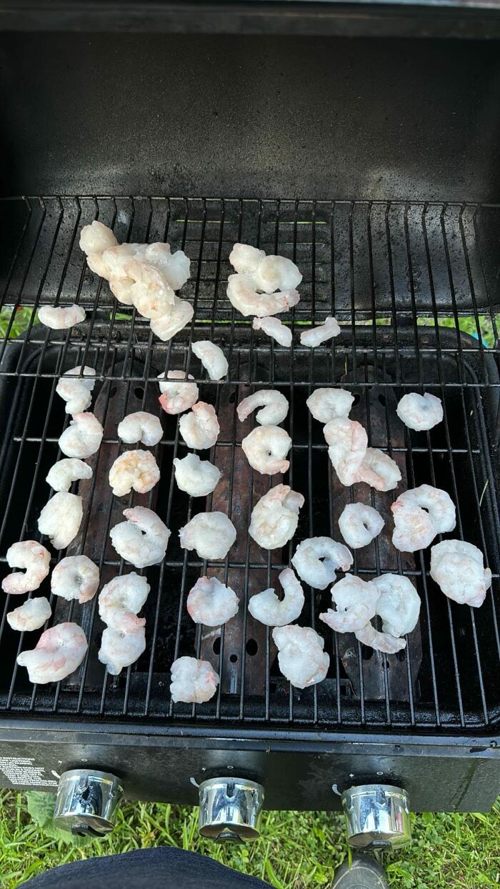 Raw shrimp scattered unevenly on a dirty grill, highlighting cursed food pics with unsettling cooking preparation.