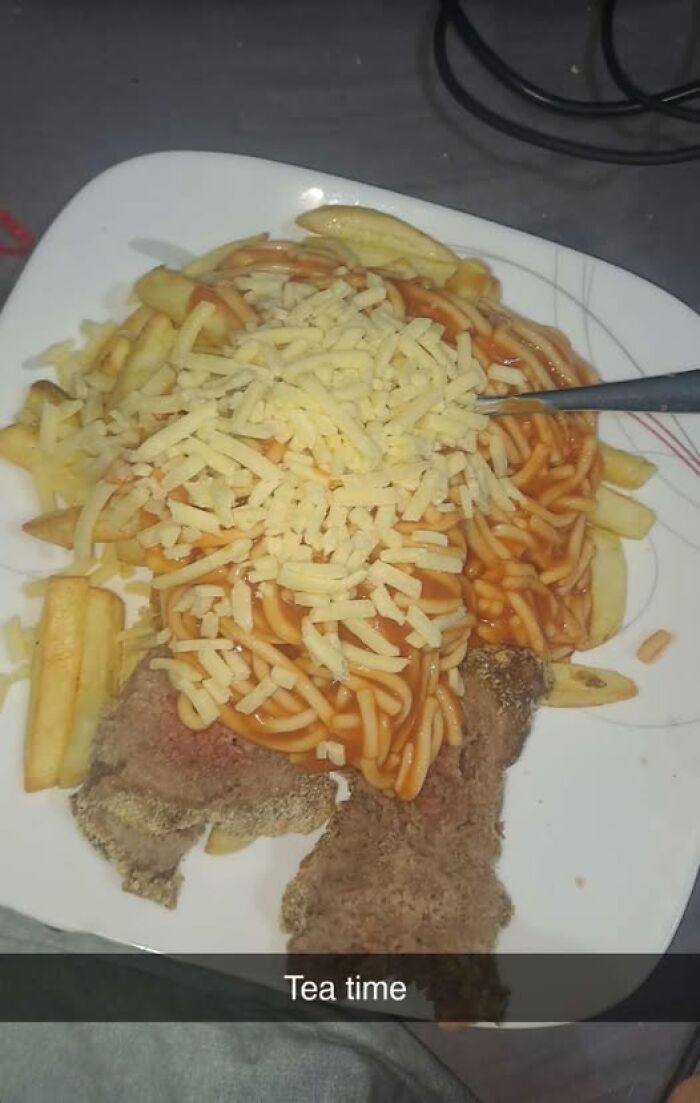 Plate of fries topped with spaghetti and shredded cheese on breaded meat, a cursed food pic that may need a trigger warning.