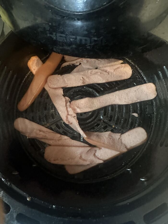 Cursed food image showing shriveled and oddly shaped hot dog slices cooking in an air fryer basket.