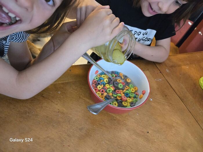 Two children pouring pickles into a bowl of colorful cereal, creating a cursed food combination.