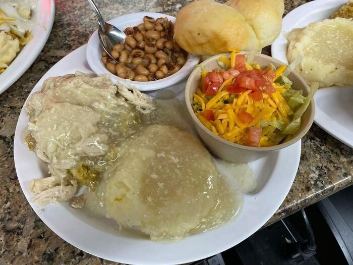 Plate of southern food including chicken with gravy, mashed potatoes, black-eyed peas, biscuit, and salad showing cursed food presentation.
