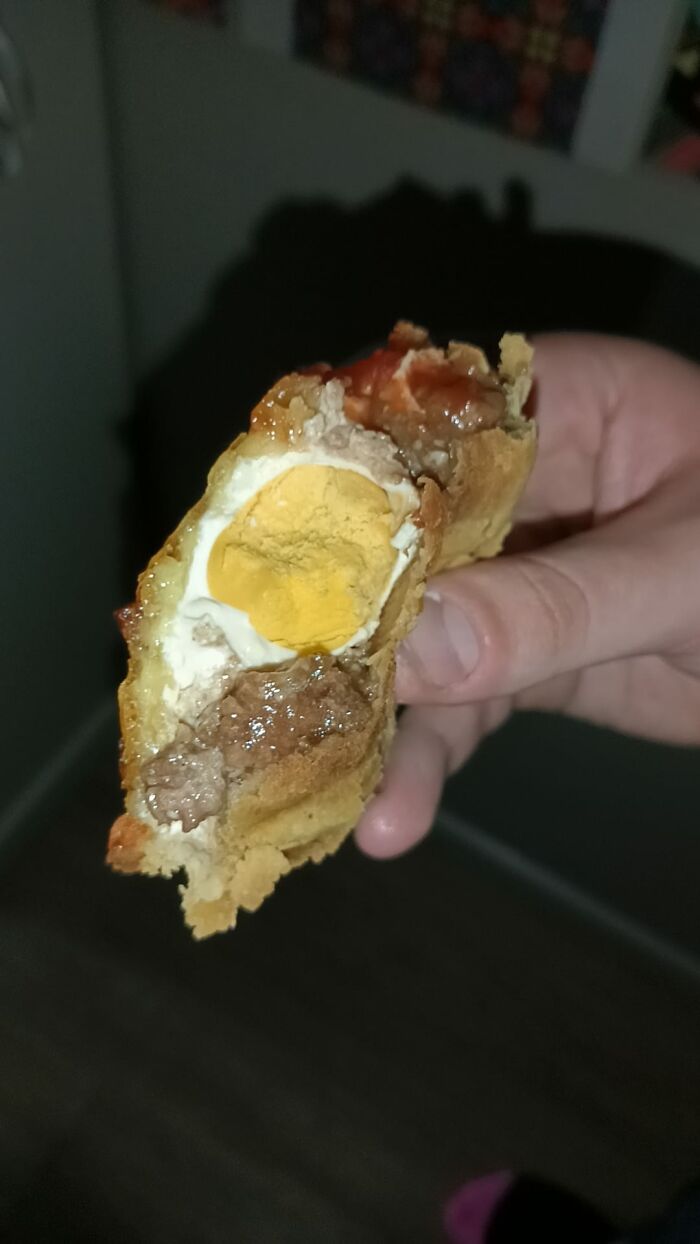 Hand holding a cursed food pic showing a slice of pie with an oddly placed hard-boiled egg inside the filling.