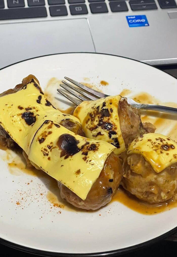 Plate with browned cheese-covered meatballs in sauce, an example of cursed food pics that may trigger discomfort.