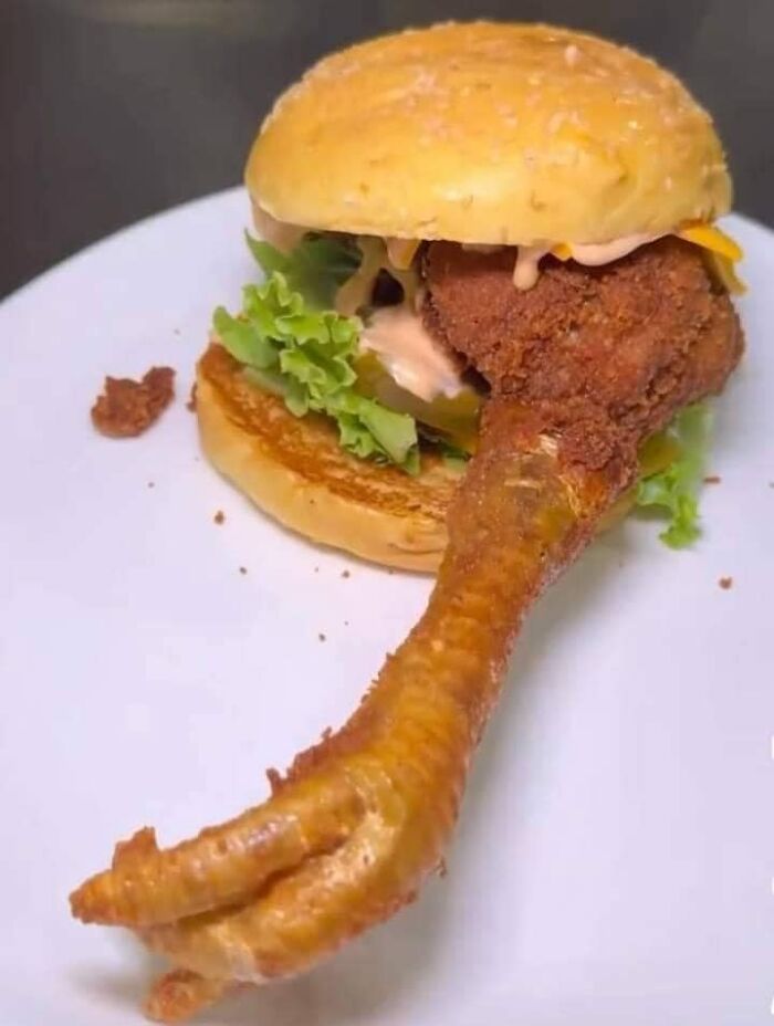 Fried chicken drumstick with claw attached in a sandwich on a white plate in a cursed food pics style.