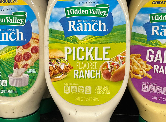 Three bottles of Hidden Valley ranch dressing in flavors including pickle, displayed in a grocery store aisle.