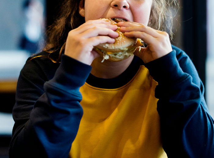 Person in a yellow and black shirt eating a burger, representing funny things foreigners say about the United States.