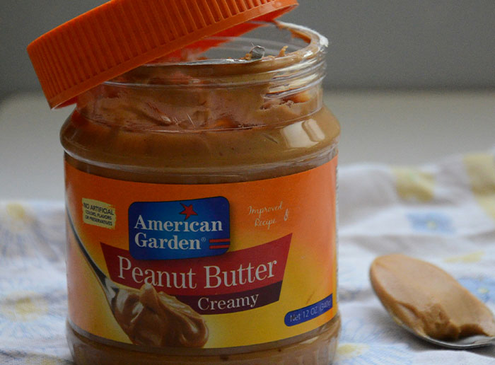 Open jar of American Garden creamy peanut butter with a spoonful of peanut butter on a cloth background.