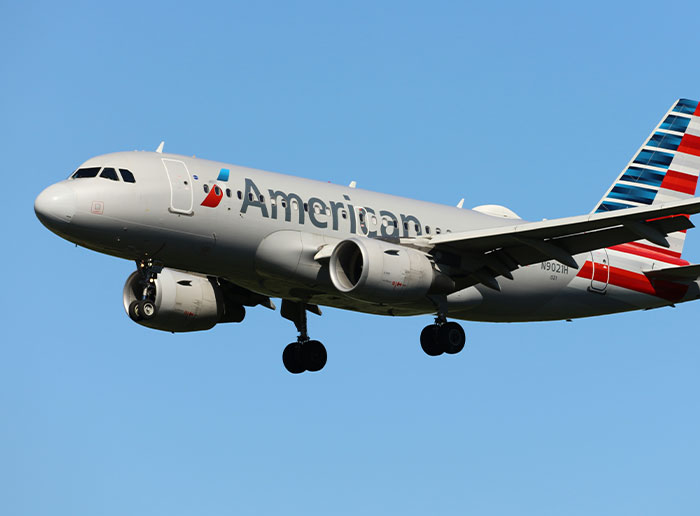 American Airlines airplane flying with clear blue sky, related to Americans and funny things foreigners say about US.