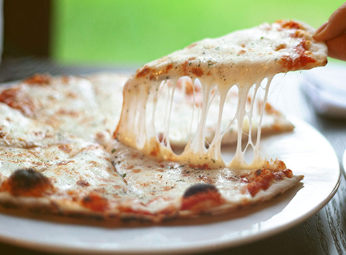 Slice of cheesy pizza being lifted from a plate, illustrating funny things foreigners say about the United States.
