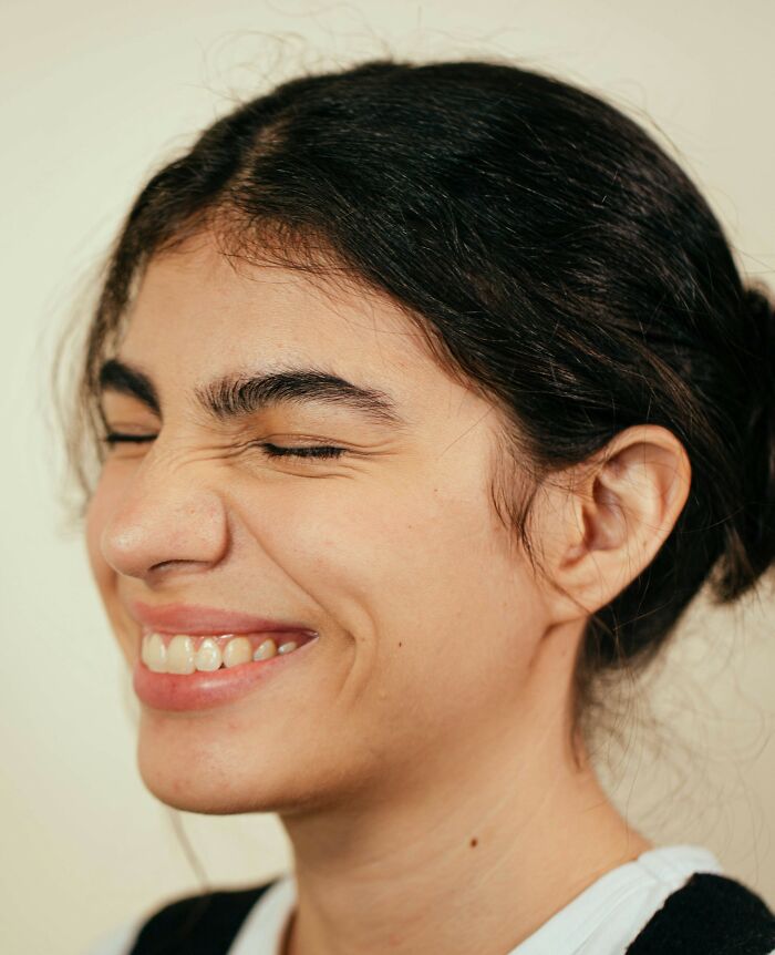 Young woman with dark hair smiling with eyes closed, showing happiness in a candid moment related to good genes.