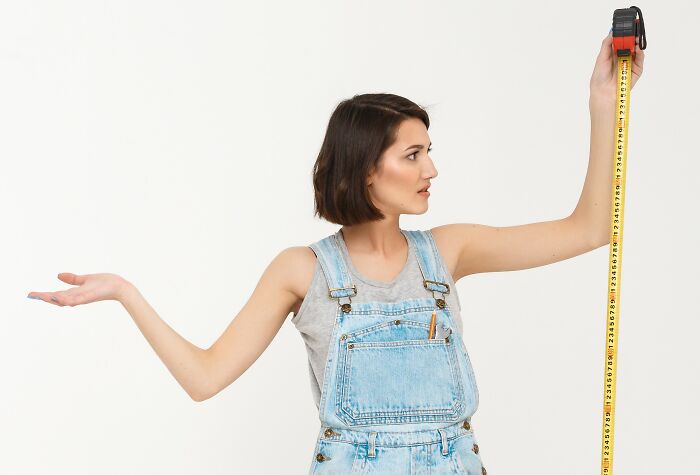 Young woman in denim overalls measuring height with tape showing body changes that indicate aging signs clearly.