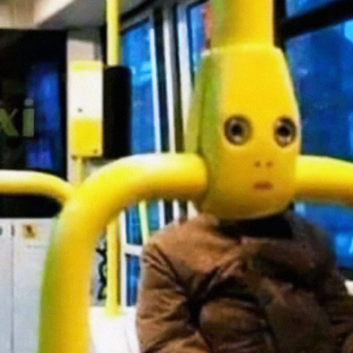 Person wearing a large yellow banana costume head with big eyes seated inside a public bus weird pics or it didn’t happen moment