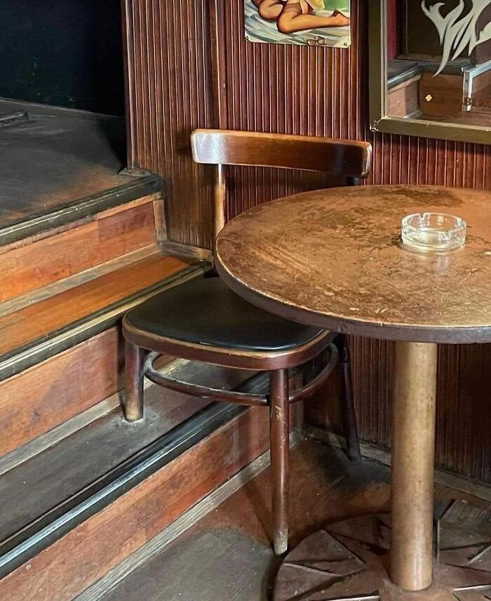 Wooden chair oddly placed on stairs next to a round wooden table with an ashtray in a rustic setting.