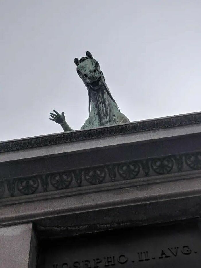 Bronze horse statue waving from a rooftop, capturing a weird pics or it didn’t happen moment on a cloudy day.