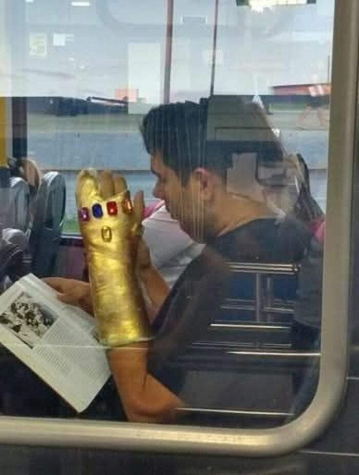 Man on a bus reading a book while wearing a large golden gauntlet with colored gems, a weird pics or it didn’t happen moment.