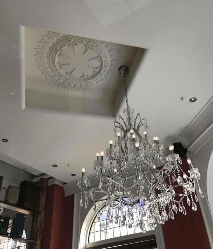 Crystal chandelier hanging in a room with a ceiling clock embedded in a recessed section, capturing a weird pics or it didn’t happen moment.