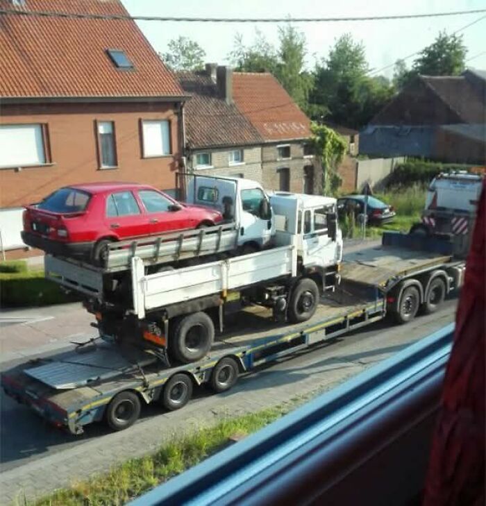 Red car carried on a small truck, which is loaded onto a larger trailer, showcasing a weird pics or it didn’t happen moment.