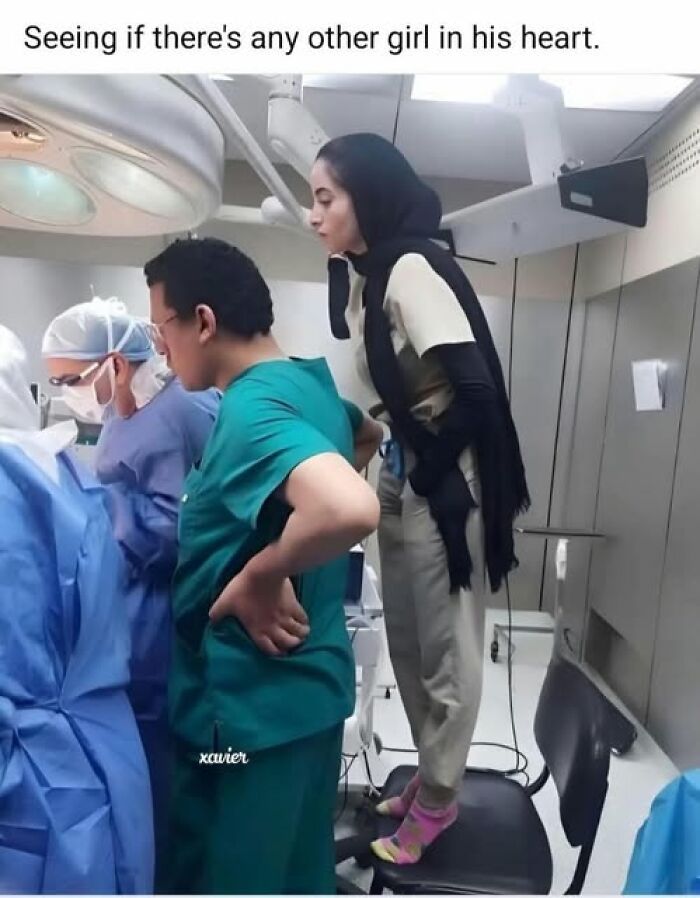 Woman standing on a chair in a medical setting, leaning to look over a man's shoulder, vegan meme humor in a hospital.