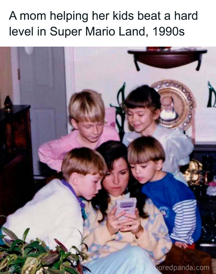 A mom and her kids focused on playing a chaotic meme-inspired game on a retro handheld console in the 1990s.