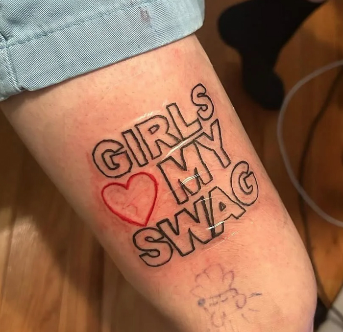 Tattoo of bold outlined text saying girls heart my swag on a person's leg, showcasing a funny and interesting tattoo design.