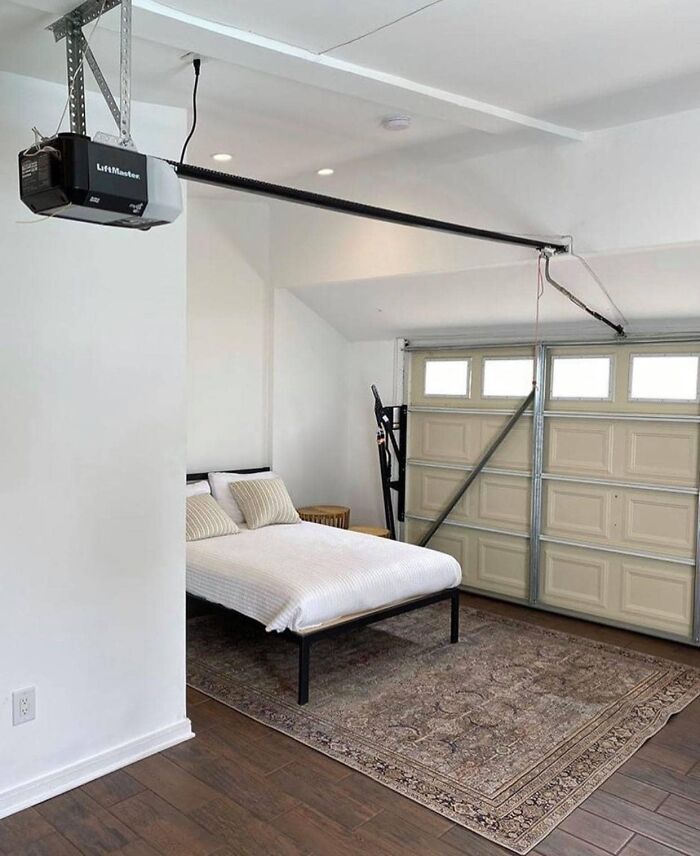 Bedroom set up inside a garage with a bed, rug, and garage door opener visible, illustrating worst real estate photos.