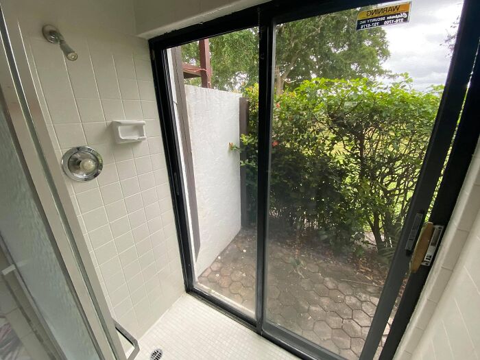 Small shower with sliding glass door opening directly onto an outdoor patio, illustrating worst real estate photos ever.