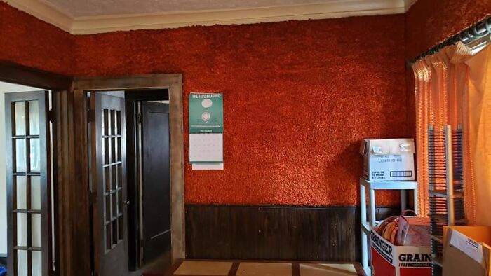 Room with textured bright orange walls, old wooden doors, and cluttered shelving in a poorly staged real estate photo.