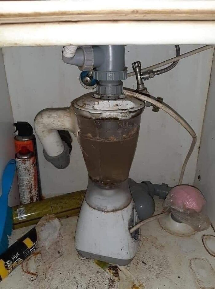 Dirty and broken kitchen garbage disposal under sink surrounded by grime and clutter in a worst real estate photo.