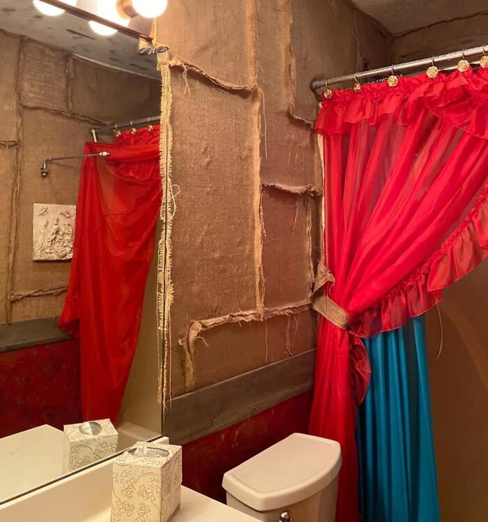 Bathroom with torn burlap walls and bright red and blue curtains in one of the worst real estate photos ever shown.