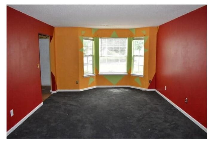 Living room with bright red and orange walls, dark carpet, and a large bay window, featured in worst real estate photos.