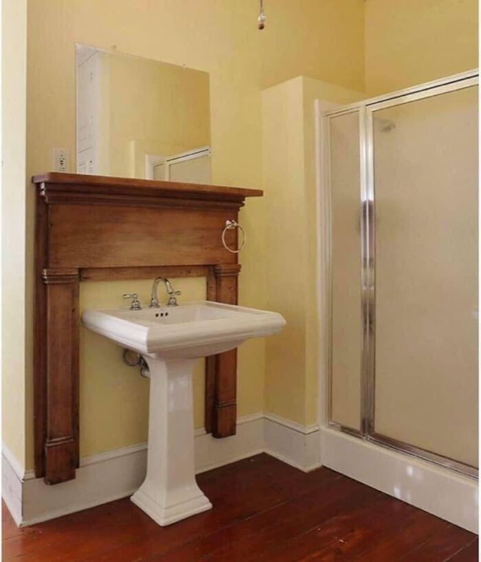 Bathroom with an awkwardly placed wooden mantle above the sink and a frosted glass shower in a real estate photo.