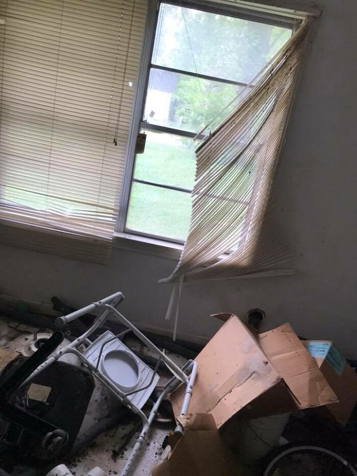 Damaged blinds and cluttered floor with a broken chair and cardboard box in a poorly maintained real estate photo.