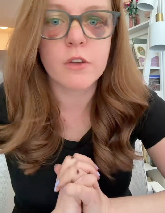 Woman with glasses and long hair speaking about misogyny and gender-based violence in an indoor setting.