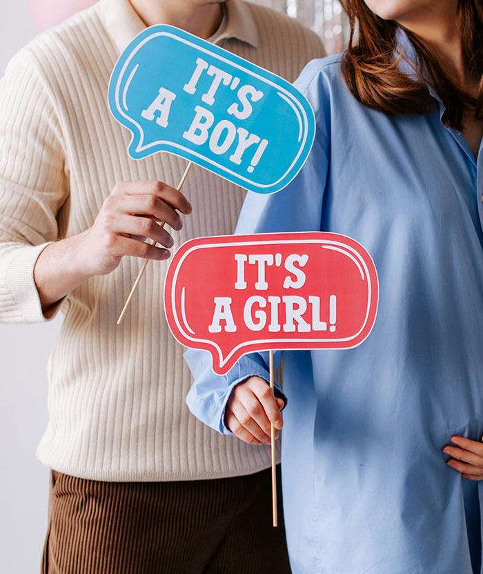 Couple holding gender reveal signs saying its a boy and its a girl during baby's gender reveal celebration event.