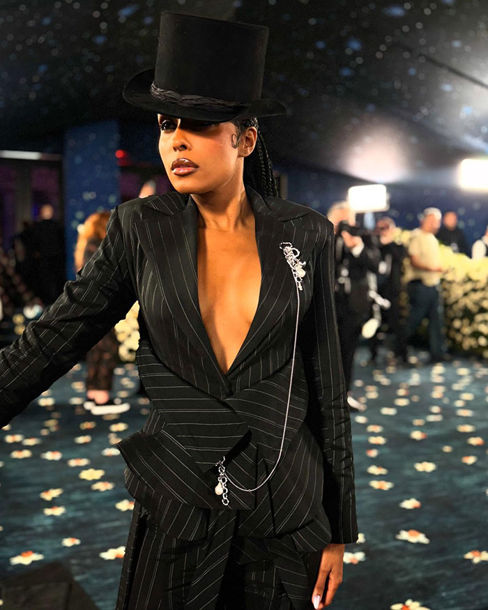 Reporter on Met Gala red carpet wearing pinstripe suit and tall hat, fans praising her for outshining celebrities. Reporter on Met Gala red carpet wearing pinstripe suit and tall hat, fans praising her for outshining celebrities.
