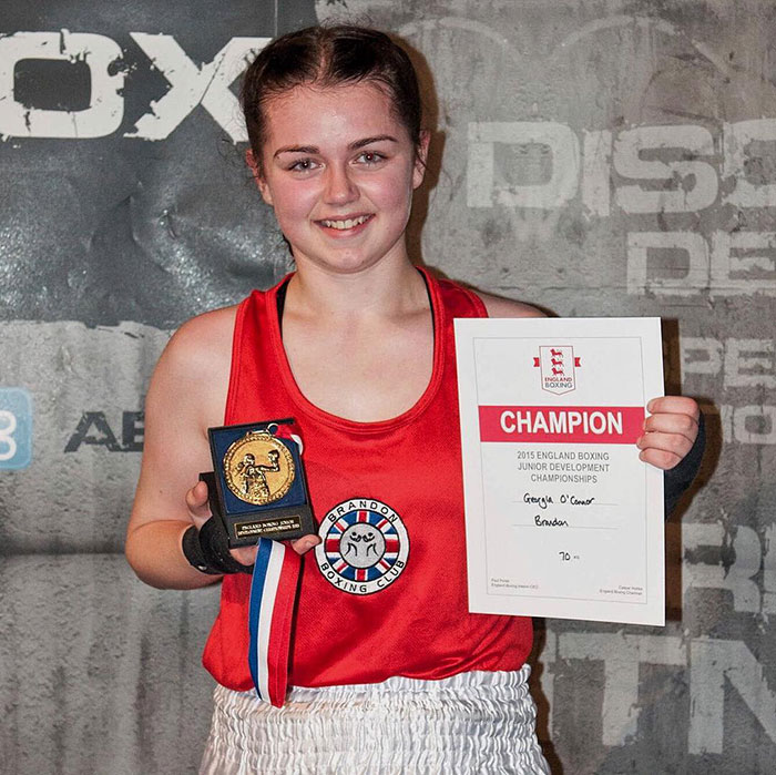 Young pro boxer Georgia O&rsquo;Connor holding champion plaque and certificate at a boxing event.