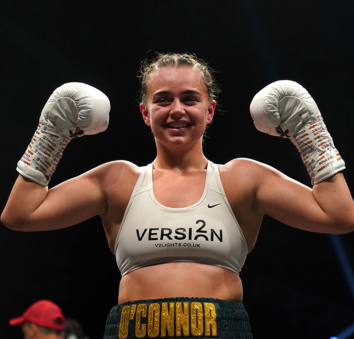 Pro boxer Georgia O&rsquo;Connor smiling and raising her gloves in victory during a professional boxing match.