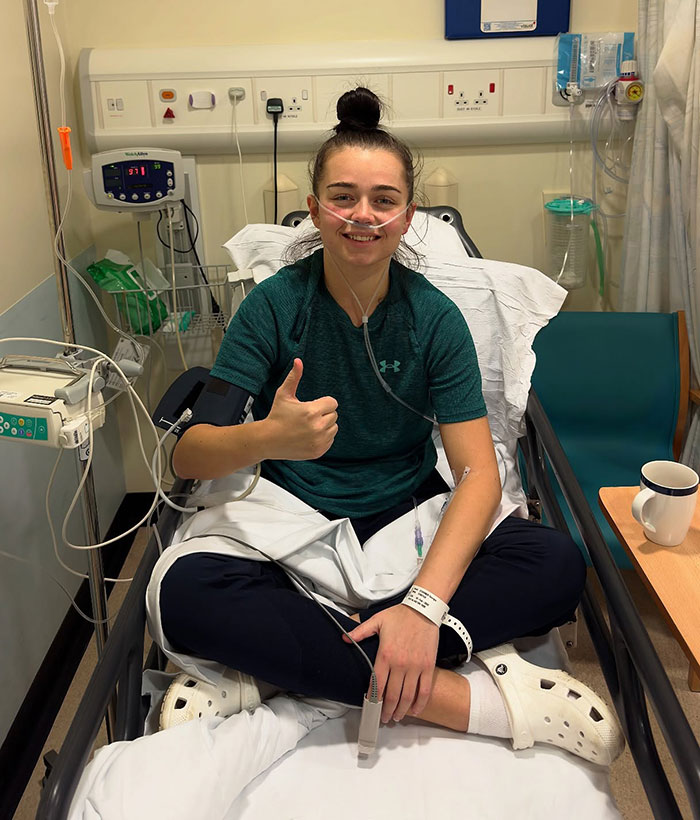 25-year-old pro boxer in hospital bed with oxygen tube, giving thumbs up during recovery.